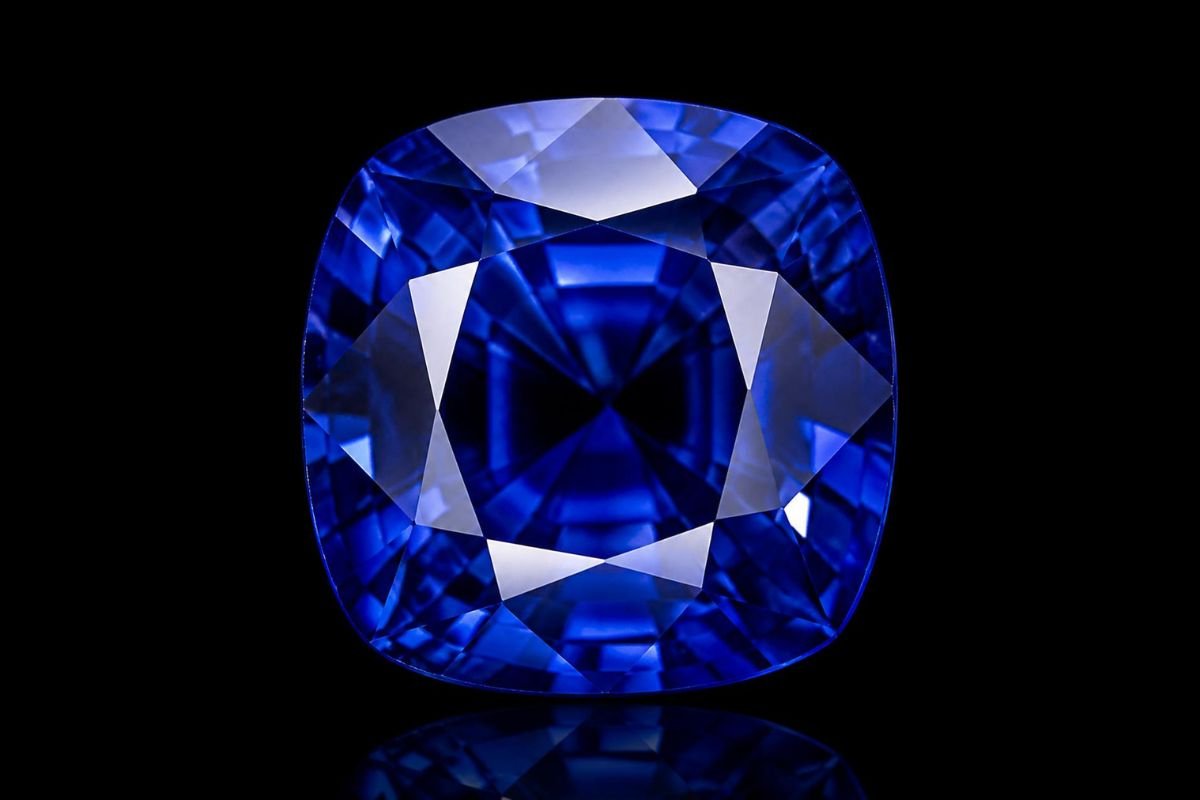 A flawless, cushion-cut royal blue Ceylon sapphire gemstone glowing against a deep, dramatic black background.